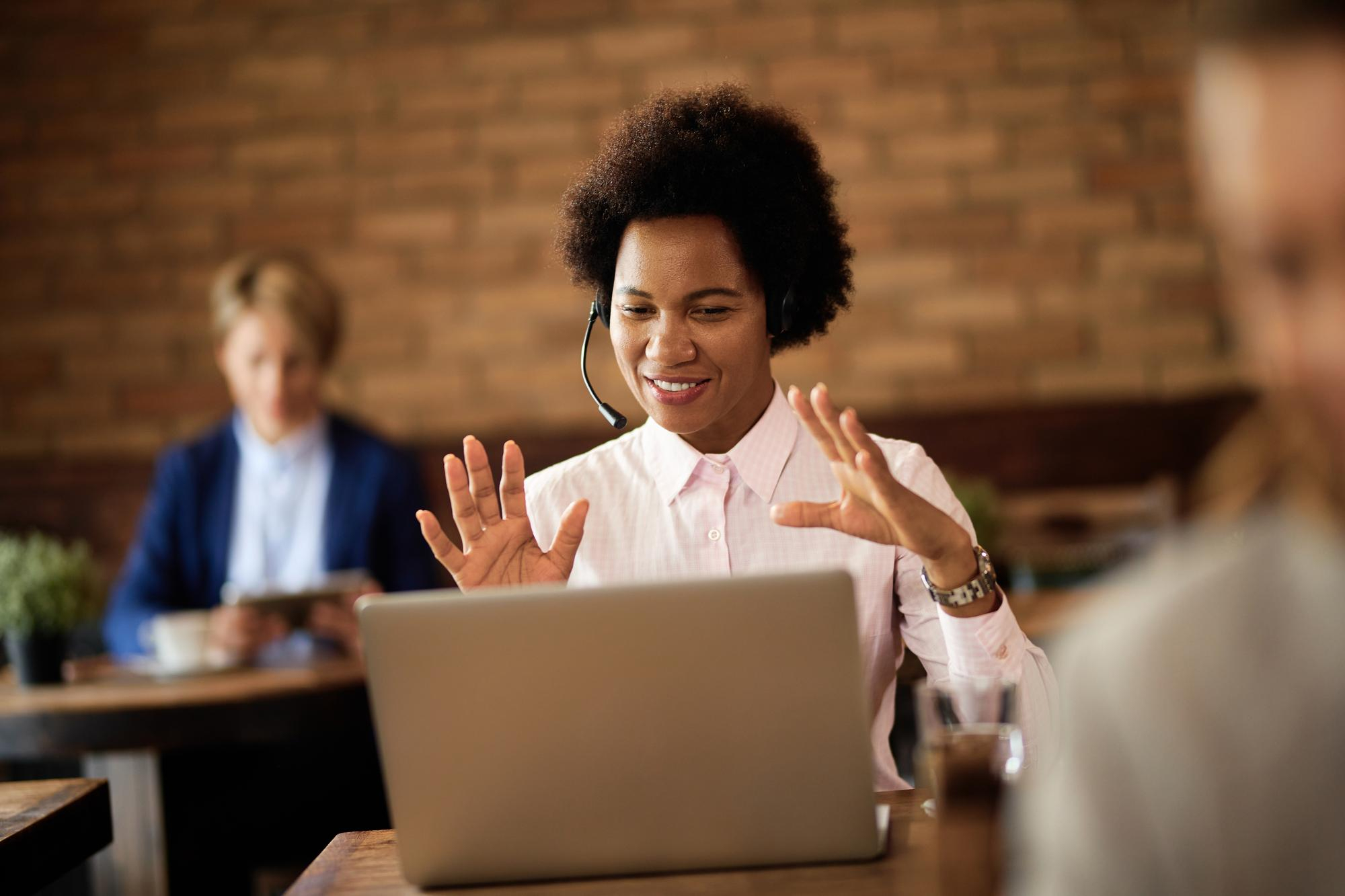Woman in a virtual meeting waving at laptop screen